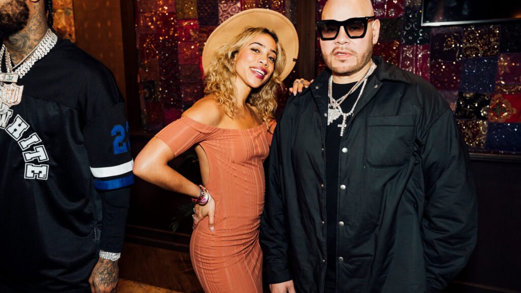 Fat Joe and a stylish attendee posing for a photo at a music festival event, with a colorful and patterned background, organised by emc3, a global events agency