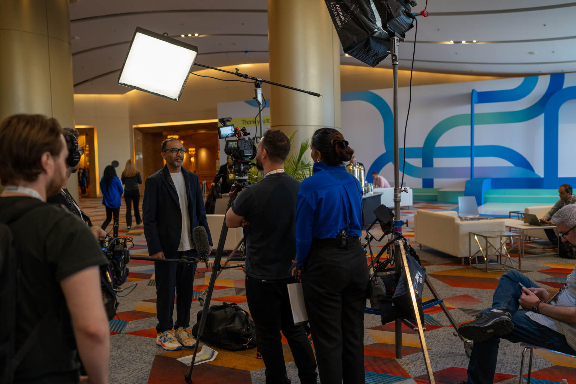 A video crew interviewing a man in a suit at the HP Amplify Partner Conference 2024 with professional lighting and camera equipment set up in a modern conference hall