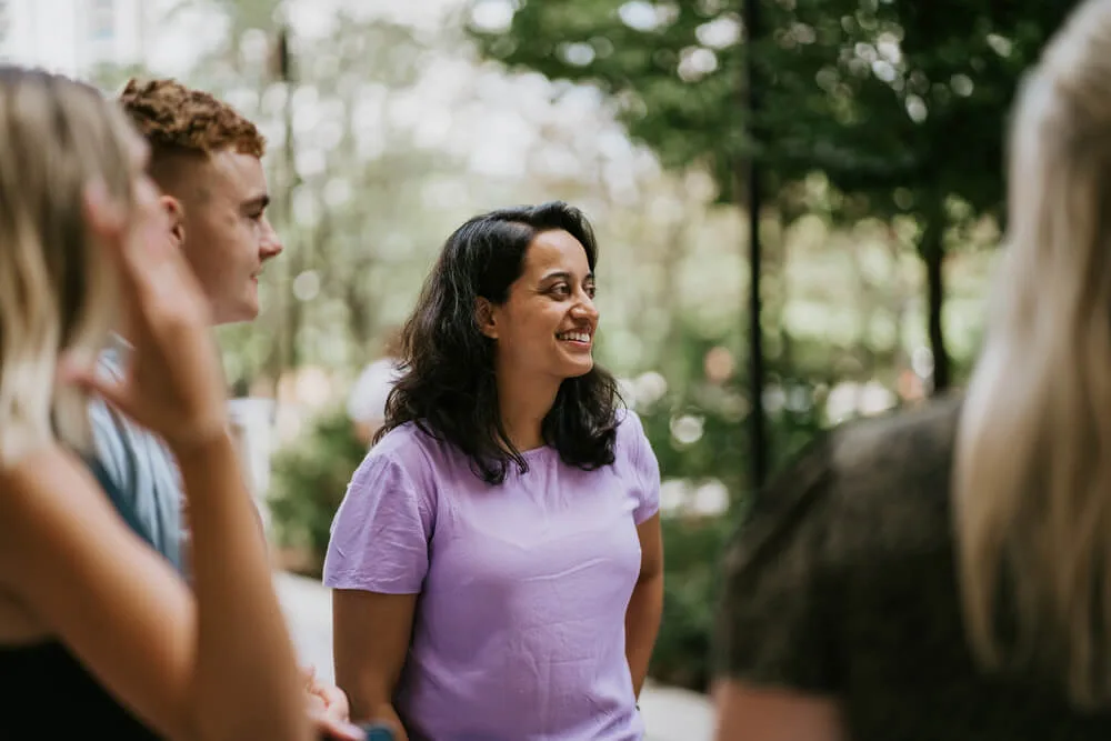 A group of people chatting outdoors with a smiling woman in a purple shirt as the central focus