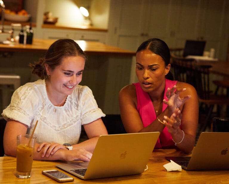 Two attendees collaborating on laptops during EMC3 event planning session