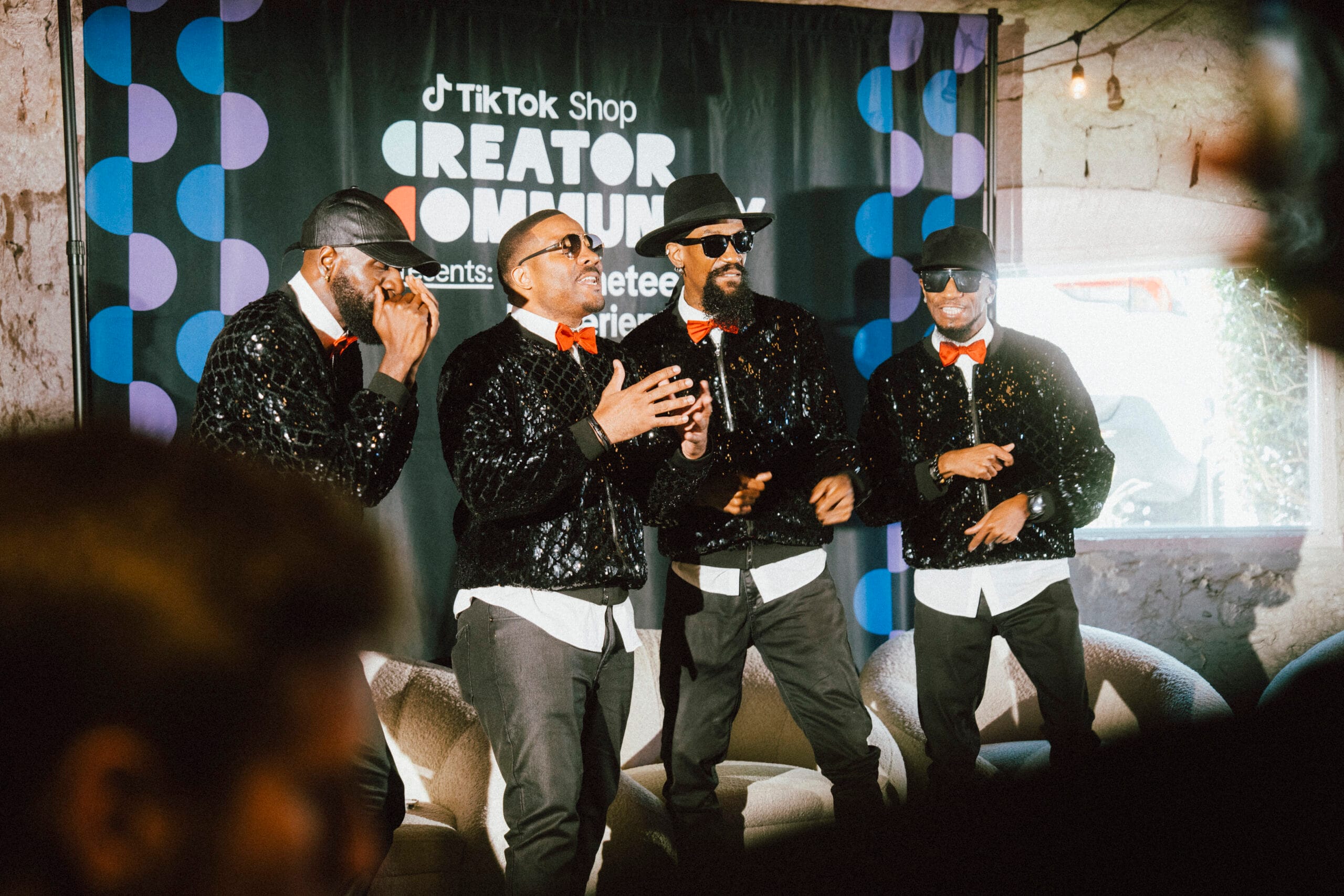 A quartet of Black male performers in coordinated black sequin jackets singing onstage at the TikTok Shop Creator Community Juneteenth event.